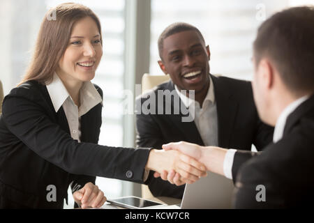 Beautiful smiling businesswoman with african american partner main tremblante et l'accueil de nouvelles entreprises, membre de l'équipe ou un demandeur d'emploi accompagnement de l'entreprise. Banque D'Images