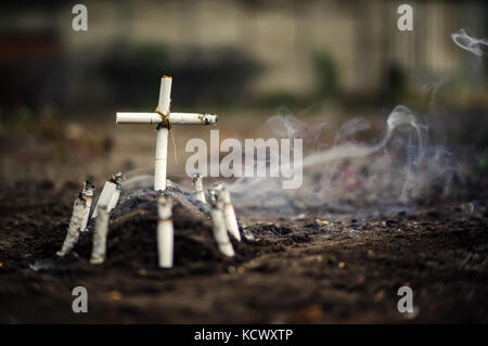 Tombe de mauvaise habitude. un anti tabac photo conceptuelle avec copyspace. tombe d'une croix faite de cigarettes et des mégots sur le sol. Banque D'Images