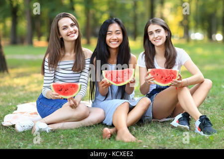 Portrait de trois belle femme avec des tranches de melon d'eau à l'extérieur. une fille asiatique et deux blancs s'amuser à pique-nique avec des fruits sur chaude journée. fr Banque D'Images