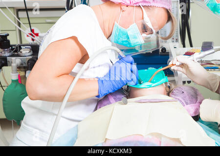 Jeune femme dentiste dans un stérile rose hat, un uniforme blanc, bleu gants stériles à usage unique et son adjointe, traiter les dents de carie dentaire Banque D'Images