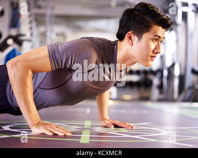 Les jeunes adultes asiatiques man exercising in gym faire push-ups, vue de côté. Banque D'Images