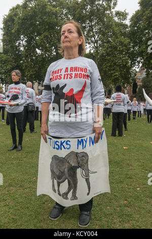 Londres, Royaume-Uni. 7 octobre 2017. Une femme est titulaire d'une affiche dans la formation diamant de gens habillés en t-shirts contre le commerce de l'ivoire avec des défenses d'éléphants maquette holding ou de rhinocéros dans une demi heure, une manifestation silencieuse à la place du Parlement comme un événement annuel dans la Marche Mondiale pour les éléphants et Rhinocéros (GMFER) prévues dans le monde entier. Orateurs à la fin de cette veillée a demandé au gouvernement britannique d'apporter à l'interdiction totale sur l'ivoire et de mettre fin au commerce par les commerçants d'antiquités en Grande-Bretagne qui joue un rôle central dans la préservation de l'ouverture des marchés de l'ivoire et la conduite que le braconnage menace de faire un éléphant Banque D'Images