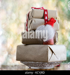 Boîtes-cadeaux enveloppées dans du papier rustique et des formes de coeur ruban et petit elfe de bois sur fond abstrait. Banque D'Images