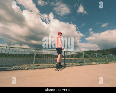 Vue arrière pour inline skater en rouge t-shirt et pantalon noir patinage sur le pont . piscine roller sur sol en béton lisse sur le lac de pont. Lig Banque D'Images