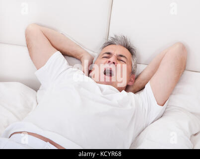 Portrait de bâillements man étend ses bras au lit Banque D'Images