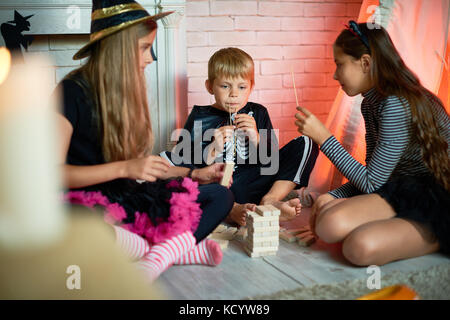 Portrait de trois enfants vêtus de costumes de Halloween, un garçon et deux filles, jouer au jeu tower studio décoré dans Banque D'Images