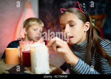 Portrait de la jolie petite fille d'allumer des bougies sur l'Halloween dans la salle décorée, little boy wearing costume en arrière-plan Banque D'Images