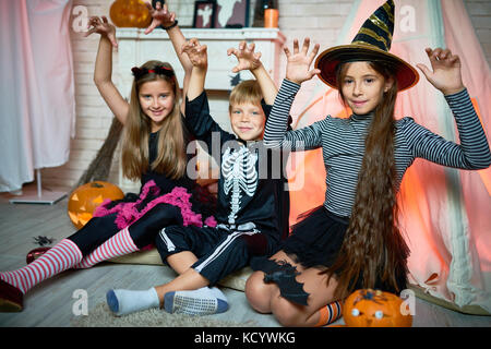 Portrait de groupe de joyeux enfants vêtus de costumes de Halloween posant pour la photographie tout en restant assis sur un sol en parquet d'un salon décoré pour maison de vacances Banque D'Images