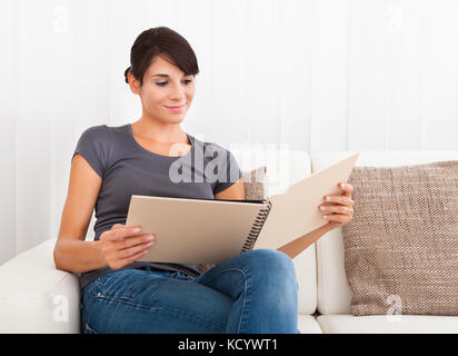 Young woman sitting on couch reading book Banque D'Images