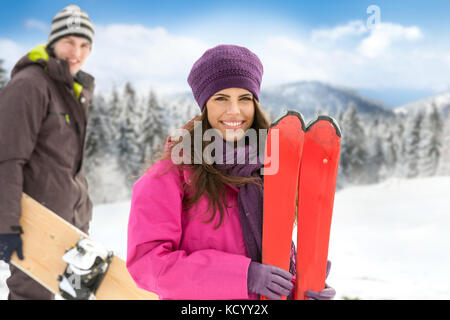 Jeune femme avec ski et snowboard avec l'homme en hiver montagne Banque D'Images