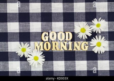 Bon matin écrit avec des lettres en bois à damier blanc sur tissu avec fleurs Daisy Banque D'Images