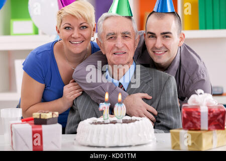 Man celebrating son anniversaire en famille, prêt à souffler les nombreuses bougies sur son gâteau. Banque D'Images