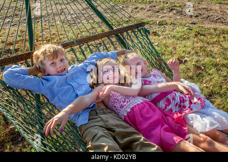 Trois enfants heureux balançant ensemble sur un hamac. Banque D'Images