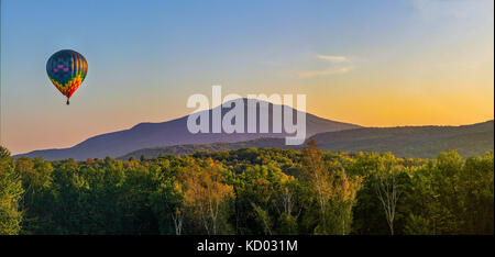 Une montgolfière colorée flotte au-dessus des arbres vers le mont Ascutney, près de Hartland, VT, USA. Banque D'Images