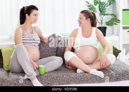 Deux femmes enceintes friends sitting on sofa at home et le partage d'expériences Banque D'Images