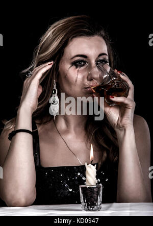 Jeune femme déprimée avec un verre de whisky sur fond noir Banque D'Images