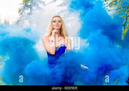 Belle jeune femme dans la forêt dans un nuage de fumée bleu vif Banque D'Images