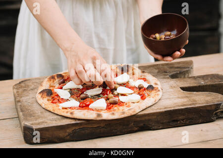 Woman putting olives sur des pizzas, mid section Banque D'Images