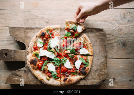 Woman taking pizza slice de pizza sur planche, overhead view Banque D'Images