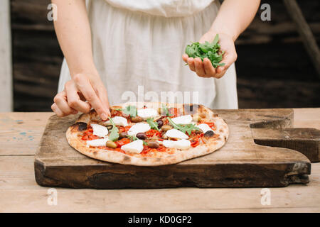 Woman putting herbs sur pizza faite maison, mid section Banque D'Images