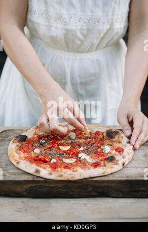 Woman putting ingrédients sur la pizza faite maison, mid section Banque D'Images