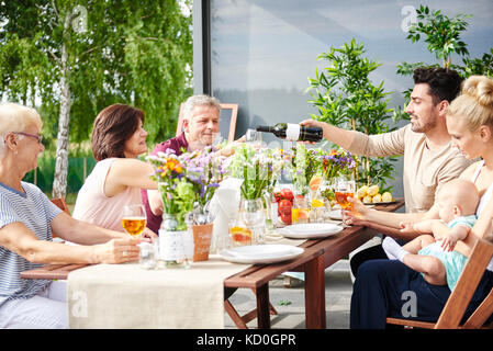 Three generation family having lunch et verser le vin sur table patio Banque D'Images