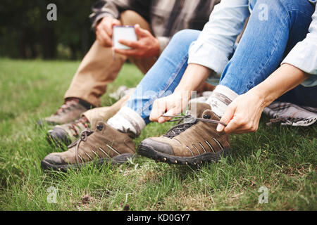 Young couple sitting on grass, femme bottes de marche de liage, low section Banque D'Images