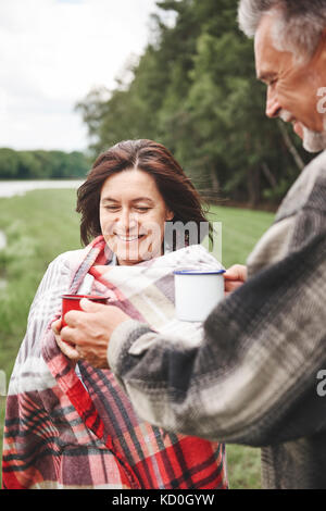 Mature couple standing in rural, holding boisson chaude, woman wrapped in blanket Banque D'Images