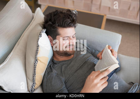 Mid adult man relaxing on sofa, reading book, elevated view Banque D'Images