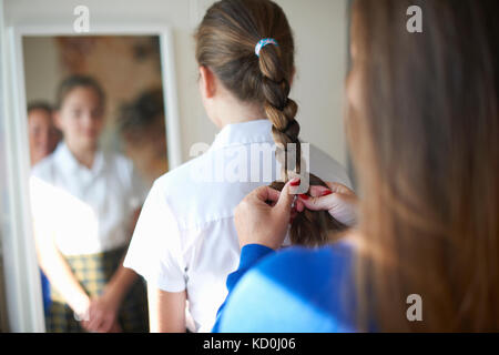 Plus d'épaule de la mère adolescente à tresser les cheveux de sa fille écolière Banque D'Images