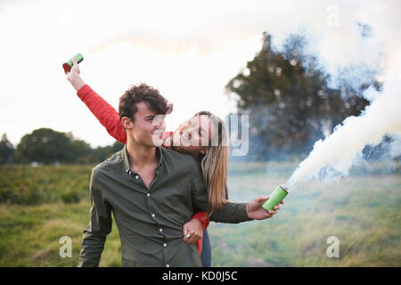 Jeune couple letting off fumigènes dans le champ Banque D'Images