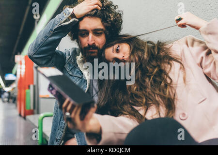 Jeune couple assis dans la gare, looking at smartphone, expressions inquiets Banque D'Images