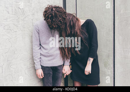 Young couple outdoors, debout contre le mur, tenant les mains, les cheveux couvrant leurs visages, Banque D'Images