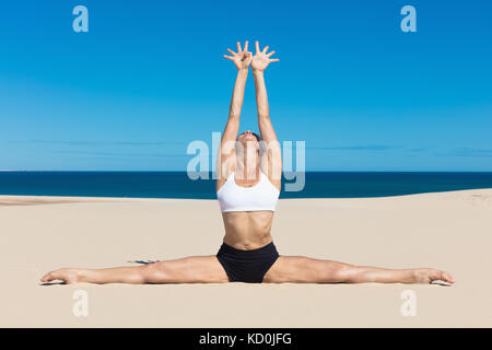 Woman on beach in yoga position, bras levés faisant le grand écart Banque D'Images