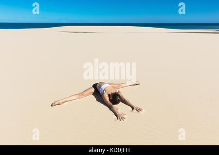 Woman on beach in yoga position, se pencher en avant de faire le grand écart Banque D'Images