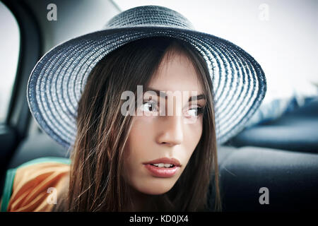 Jeune femme en chapeau à la voiture sur le côté de la banquette arrière Banque D'Images