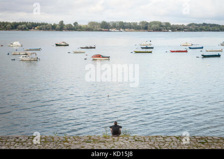 Belgrade, Serbie - septembre 3, 2017 : jeune homme assis et regarder les bateaux de pêche sur le quai de Zemun (zemunski kej) en un après-midi nuageux sur le Danube Banque D'Images