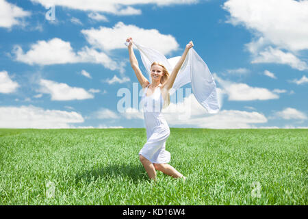 Young woman running in field holding un morceau de tissu blanc Banque D'Images