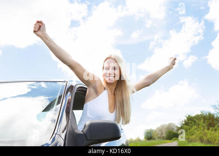 Happy young woman raising hand out of car window Banque D'Images