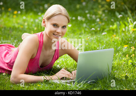 Happy Woman Lying On Grass Using Laptop Banque D'Images