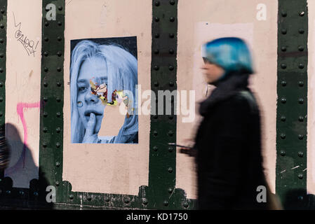 Femme floue avec des cheveux bleus en passant devant un mur avec le street art photographie murale portrait de jeune enfant à Brick Lane, Shoreditch, East London, UK Banque D'Images