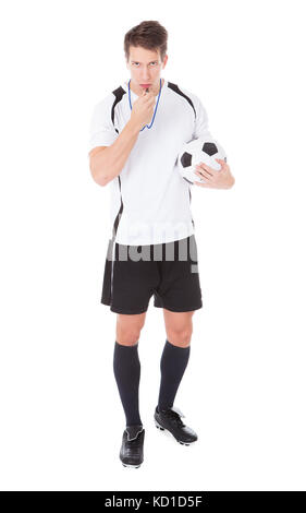 Portrait de jeune homme arbitre Soccer Holding Football et soufflant sifflent Banque D'Images