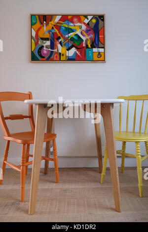 La consommation de l'espace montrant inspiré scandinave table avec top blanc et pieds en bois peint de couleurs vives, des chaises, mur peint blanc et pièce d'art abstrait Banque D'Images