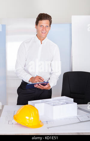 Architect looking at architectural model writing on clipboard Banque D'Images