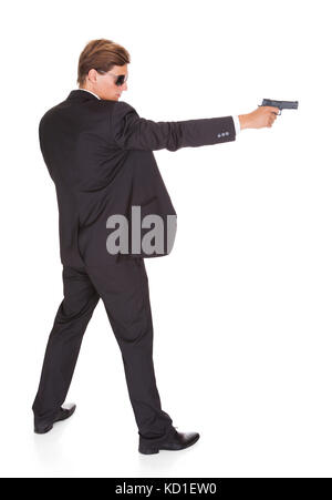 Jeune homme en costume noir visant avec un fusil sur fond blanc Banque D'Images