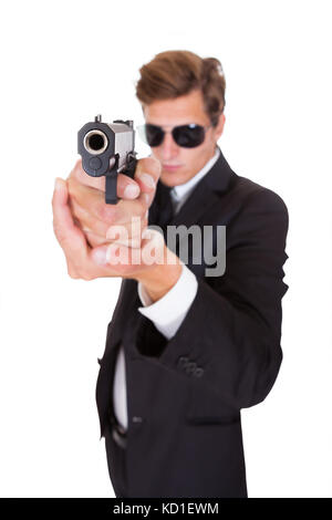 Jeune homme en costume noir visant avec un fusil sur fond blanc Banque D'Images