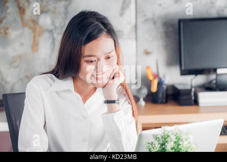 Asian businesswoman looking at laptop computer et visage souriant et de repos avec des professionnels de l'émotion à partir de la bonne nouvelle de la réussite commerciale dans la maison de Banque D'Images