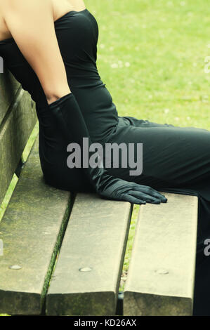 Gros plan d'une jeune femme portant une robe noire et des gants assis sur le banc à l'extérieur Banque D'Images