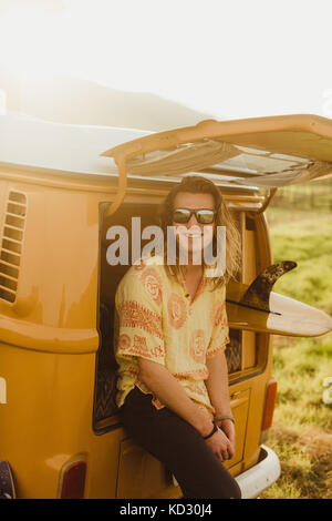 Portrait de jeune homme aux longs cheveux surfeur appuyé contre vintage véhicule récréatif, Exeter, California, USA Banque D'Images