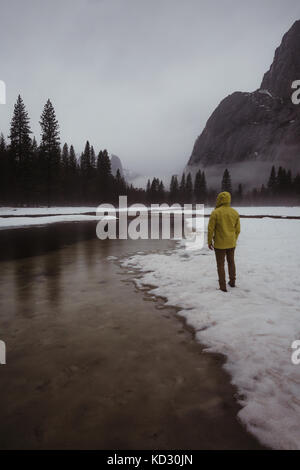 Vue arrière du male hiker surplombant le paysage couvert de neige et la rivière, Yosemite Village, California, USA Banque D'Images